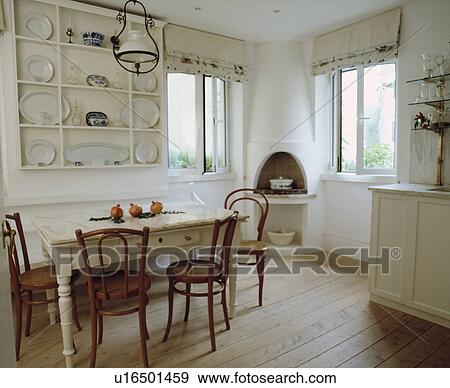 Stock Photo - White plates on white shelves in white dining room with with wooden flooring and bentwood chairs and old white table. Fotosearch