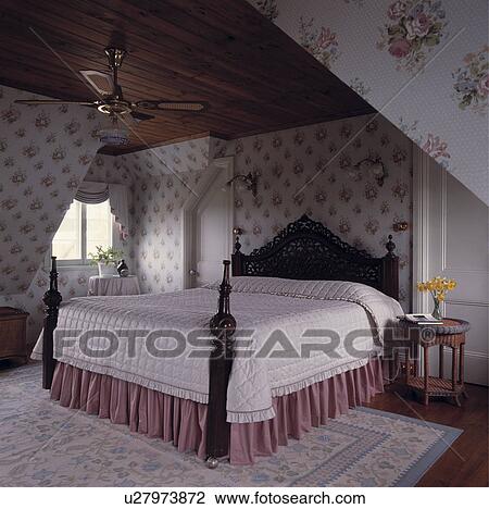 White quilt and pink vallance on carved mahogany bed with turned posts in attic bedroom with floral wallpaper View Large Photo Image Stock Image - White quilt and pink vallance on carved mahogany bed with turned posts in attic bedroom with floral wallpaper. Fotosearch