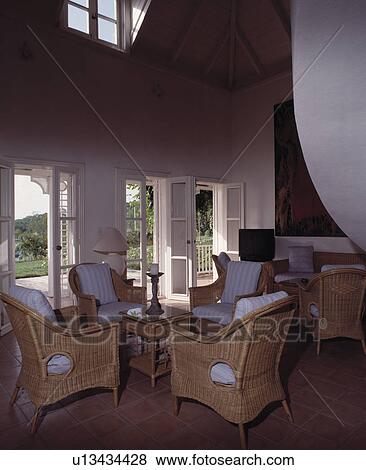 Wicker armchairs with white cushions in double height living room with French doors onto patio View Large Photo Image Stock Photo - Wicker armchairs with white cushions in double height living room with French doors onto patio. Fotosearch