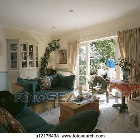 Wicker sofa with blue cushions in living room with white tiled floor and French windows open to the patio View Large Photo Image Stock Photo - Wicker sofa with blue cushions in living room with white tiled floor and French windows open to the patio. Fotosearch