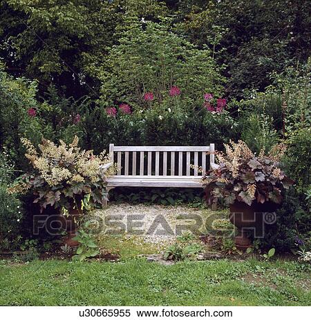Stock Photography - Wooden bench and heucheras in pots in large country garden in summer. Fotosearch