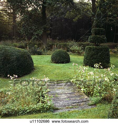 Wooden bridge across stream to lawn with clipped topiary shrubs in large country garden View Large Photo Image Stock Photograph - Wooden bridge across stream to lawn with clipped topiary shrubs in large country garden. Fotosearch