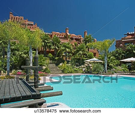 Stock Photography - Wooden bridge beside turquoise swimmingpool in gardens of Spanish holiday village. Fotosearch