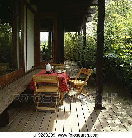 Stock Photo - Wooden chairs and table with red cloth on decked veranda of modern country house. Fotosearch