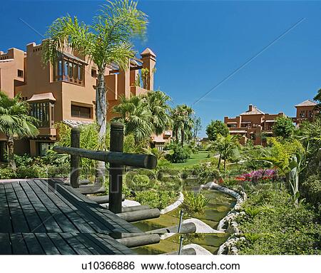Wooden decking above man-made stream in garden of terracotta apartment blocks in Spain View Large Photo Image Stock Photograph - Wooden decking above man-made stream in garden of terracotta apartment blocks in Spain. Fotosearch
