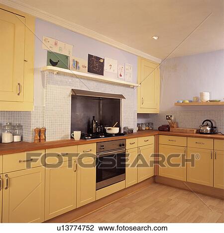 Stock Image - Wooden flooring and stainless steel oven in pastel mauve kitchen with yellow fitted cupboards. Fotosearch