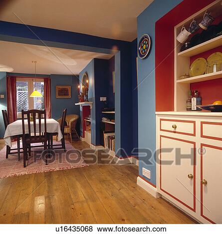 Stock Photo - Wooden flooring in blue dining room with built-in white dresser with red details. Fotosearch