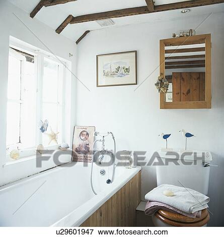 Stock Photo - Wooden mirror above toilet in white bathroom with panelled bath. Fotosearch