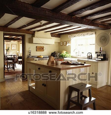 Wooden step-stool at island unit in cream cottage kitchen with beamed ceiling and wooden flooring View Large Photo Image Stock Photo - Wooden step-stool at island unit in cream cottage kitchen with beamed ceiling and wooden flooring. Fotosearch