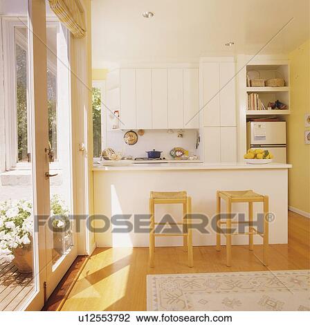 Wooden stools at breakfast bar beside patio doors in modern white kitchen View Large Photo Image Stock Image - Wooden stools at breakfast bar beside patio doors in modern white kitchen. Fotosearch