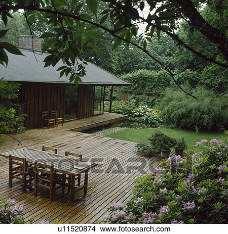 Wooden table and chairs on decking in large country garden in summer View Large Photo Image Picture - Wooden table and chairs on decking in large country garden in summer. Fotosearch