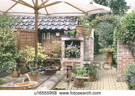 Stock Photo - Wooden table below white parasol in small courtyard in country garden. Fotosearch