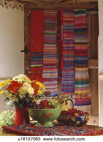 Yellow and red flowers in red jug and fruit in green bowl on table in dining room with display of mult-coloured striped scarves on the wall View Large Photo Image Stock Photography - Yellow and red flowers in red jug and fruit in green bowl on table in dining room with display of mult-coloured striped scarves on the wall. Fotosearch