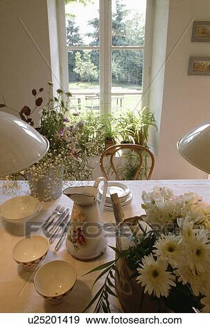 Yellow daisies and floral jug with white bowls on dining table with view of garden through window View Large Photo Image Stock Photo - Yellow daisies and floral jug with white bowls on dining table with view of garden through window. Fotosearch