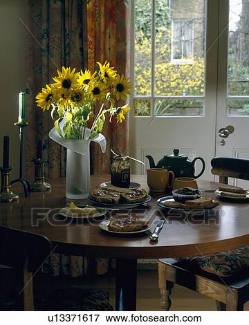 Yellow sunflowers on circular wooden dining table set for tea with view of garden through French windows View Large Photo Image Stock Photo - Yellow sunflowers on circular wooden dining table set for tea with view of garden through French windows. Fotosearch