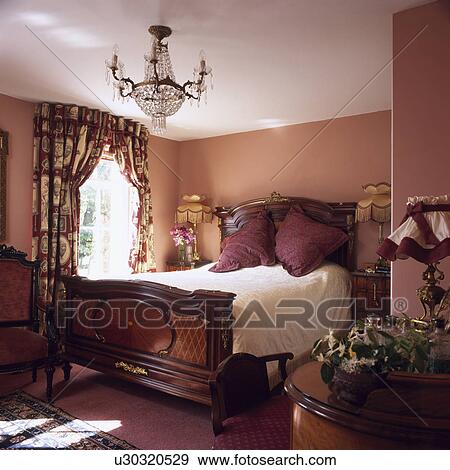 Antique Mahogany Bed And Floral Curtains In Small Dark Pink Bedroom With Antique Glass Chandelier Stock Photo