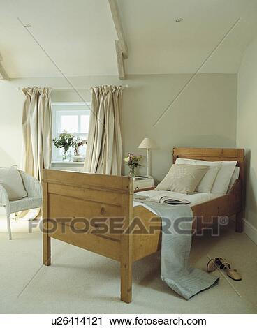 Stock Image - Antique pine single bed in corner of white attic bedroom with white carpet. Fotosearch