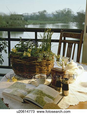 Stock Image - Binoculars and basket of spring flowers on table on veranda overlooking river. Fotosearch