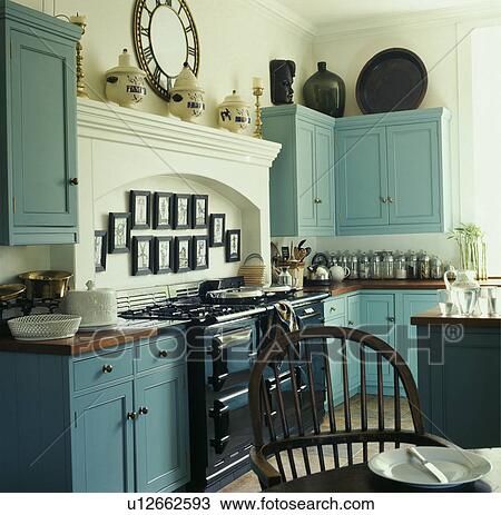 Stock Image - Black Aga below white mantelpiece in traditional white kitchen with turquoise fitted cupboards. Fotosearch