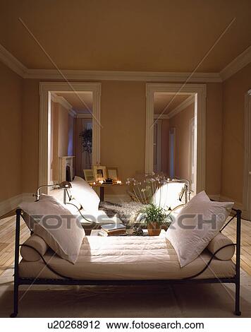 Black iron daybed with large white cushions and bolstered in uncluttered neutral bedroom with lighted floor-lamps View Large Photo Image Stock Image - Black iron daybed with large white cushions and bolstered in uncluttered neutral bedroom with lighted floor-lamps. Fotosearch
