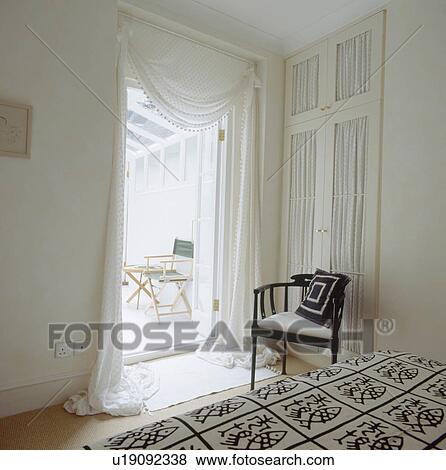 Stock Photo - Black & white cushion on modern black chair in white bedroom with white voile drapes on door to conservatory. Fotosearch