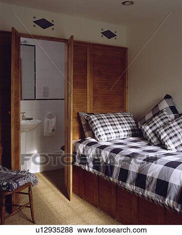 Black+white checked quilt and cushions on bed in front of wooden louvre doors to small ensuite bathroom View Large Photo Image Stock Photo - Black+white checked quilt and cushions on bed in front of wooden louvre doors to small ensuite bathroom. Fotosearch
