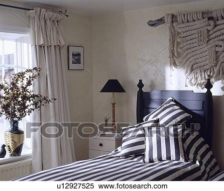 Black+white striped cushions on black single bed below knitted wallhanging in white bedroom with white curtains View Large Photo Image Stock Photography - Black+white striped cushions on black single bed below knitted wallhanging in white bedroom with white curtains. Fotosearch