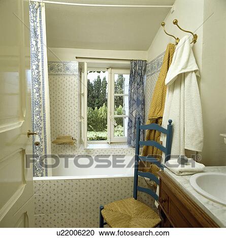 Blue ladderback chair in blue+white tiled country bathroom with bath in front of open window and bathrobes on hooks View Large Photo Image Stock Image - Blue ladderback chair in blue+white tiled country bathroom with bath in front of open window and bathrobes on hooks. Fotosearch