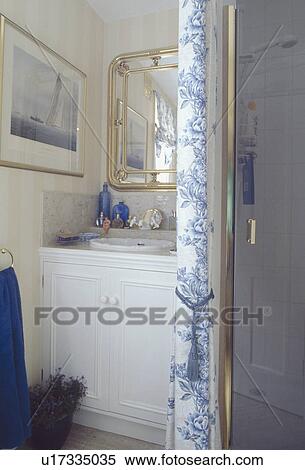 Stock Photography - Blue & white curtain beside shower door in small bathroom with mirror above basin in vanity unit. Fotosearch