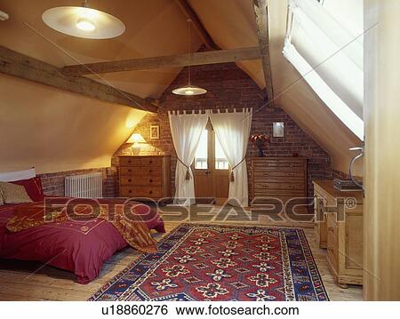 Blue Red Oriental Rug On Wooden Floor In Large Attic Bedroom With White Curtains And Red Duvet Stock Photograph