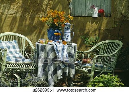 Stock Image - Blue+white cloth and pots on table in front of old stone wall in country garden in summer. Fotosearch