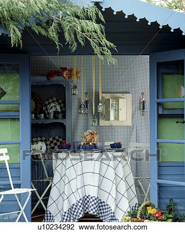 Stock Image - Blue+white cloth on table in front of blue summerhouse in country garden in summer. Fotosearch