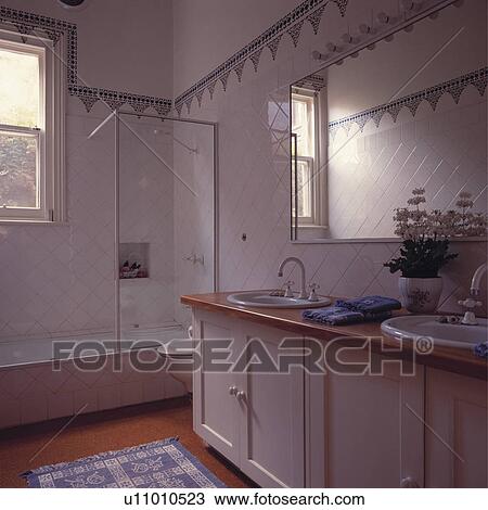 Blue+white tiled border above white tiled walls in white bathroom with double basins in traditional white vanity unit View Large Photo Image Stock Image - Blue+white tiled border above white tiled walls in white bathroom with double basins in traditional white vanity unit. Fotosearch