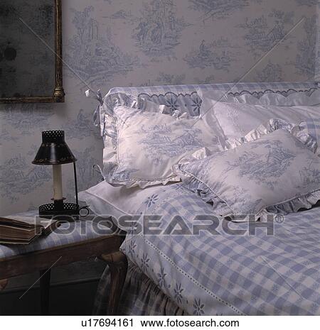 Stock Image - Blue+white toile de Jouy wallpaper above bed with matching Toile de Jouy pillows and blue+white checked duvet. Fotosearch