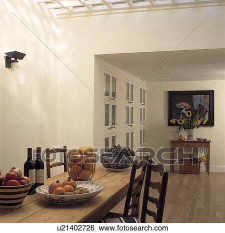 Bowls of fruit on wooden table with ladderback chairs in modern white dining room extension View Large Photo Image Stock Photograph - Bowls of fruit on wooden table with ladderback chairs in modern white dining room extension. Fotosearch