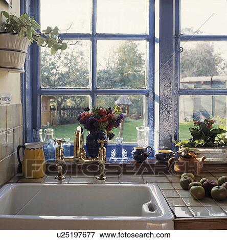 Brass mixer taps and white Butler's sink below blue window with view of garden View Large Photo Image Stock Photo - Brass mixer taps and white Butler's sink below blue window with view of garden. Fotosearch