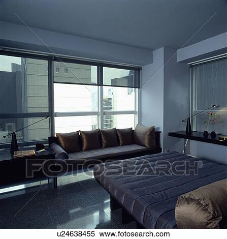 Brown silk bolster on bed with blue fitted quilt in modern city bedroom with sofa in front of large window View Large Photo Image Stock Photography - Brown silk bolster on bed with blue fitted quilt in modern city bedroom with sofa in front of large window. Fotosearch