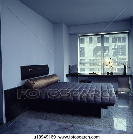 Brown silk bolster on bed with fitted blue quilt in modern apartment bedroom with see-through blind at large window View Large Photo Image Stock Photo - Brown silk bolster on bed with fitted blue quilt in modern apartment bedroom with see-through blind at large window. Fotosearch
