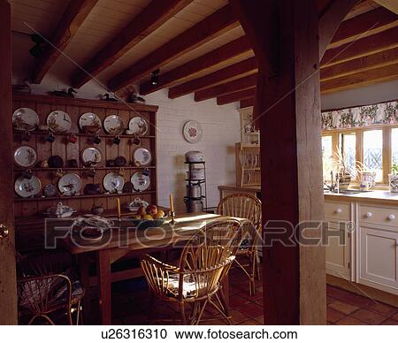 Stock Image - Cane chairs and pine table in cottage kitchen with pine dresser and beamed ceiling. Fotosearch