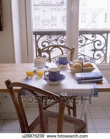 Stock Photo - Chair and blue+white spotted cups and checked cloth on table in front of French windows. Fotosearch