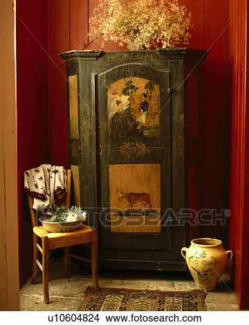 Picture - Chair beside green wooden antique cupboard with painted scenes in red hall . Fotosearch