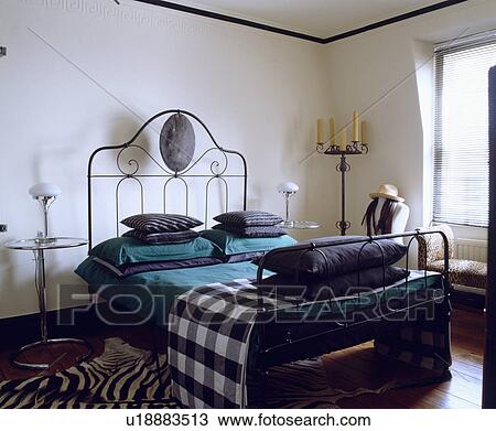 Checked throw and turquoise pillows on modern wrought metal bed in white bedroom with Eileen Gray tables View Large Photo Image Stock Image - Checked throw and turquoise pillows on modern wrought metal bed in white bedroom with Eileen Gray tables. Fotosearch