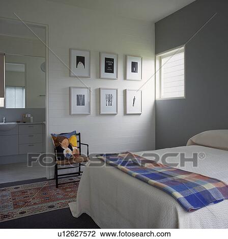 Stock Image - Checked throw on white bed in white and grey modern bedroom with black+white pictures on wall . Fotosearch