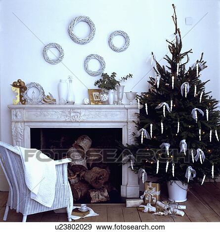 Stock Photo - Christmas tree and white Lloyd Loom chair beside fireplace in white living room. Fotosearch