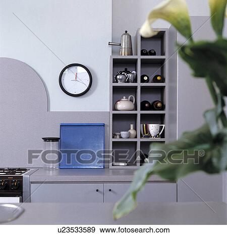 Circular clock beside coffee pot and teapots on cube shelves in pale grey kitchen with blue tray on worktop View Large Photo Image Stock Photo - Circular clock beside coffee pot and teapots on cube shelves in pale grey kitchen with blue tray on worktop. Fotosearch