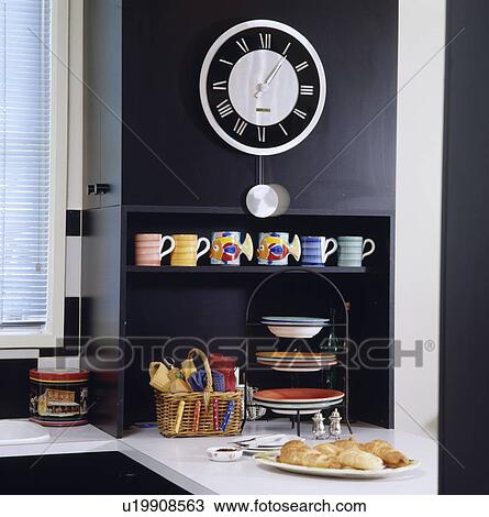 Circular clock on black wall above shelf with colourful pottery cups and cakestand View Large Photo Image Stock Image - Circular clock on black wall above shelf with colourful pottery cups and cakestand. Fotosearch