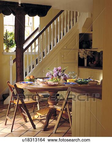 Picture - Circular dining table and wooden chairs in small cream hall with staircase in traditional country house. Fotosearch