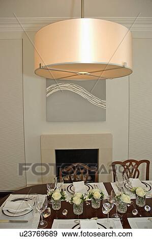 Stock Photo - Circular lampshade over table with place settings and cream roses in glass vases in modern dining room. Fotosearch