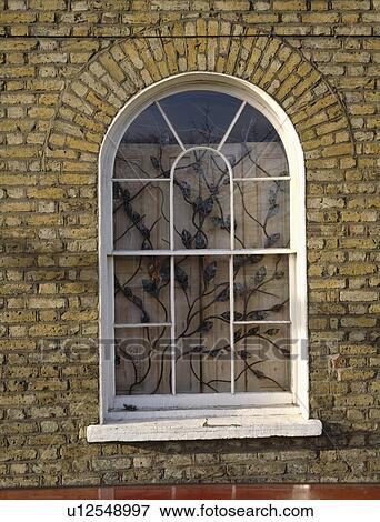 Stock Photo - Close up of arched window with interior security grille and wooden shutters. Fotosearch