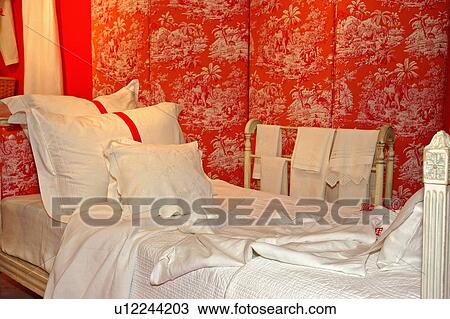 Stock Image - Close-up of bed with white linen and pillows against orange toile-de-jouy folding screen. Fotosearch